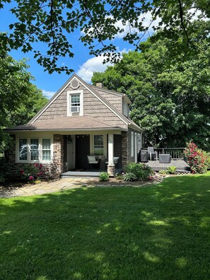 A two-story house with a stone facade, a front porch with outdoor furniture, and a well-maintained garden. - Cottage in Sugarcreek with Hot Tub (Sugarcreek)