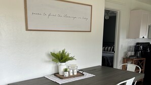 A dining area with a long table, white chairs, a small plant, and a sign on the table. - Cottage in Sugarcreek with Hot Tub (Sugarcreek)