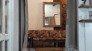 A room with a stone-tiled floor, a wooden bench, a mirror, and a small shelf with decorative items. - Casa Jardim Secreto II (Penha)