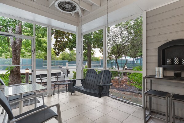 A covered patio with a grill, seating, and a view of the outdoors.