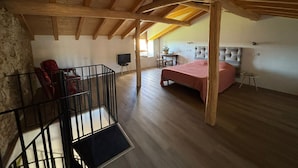 Ein geräumiges Zimmer mit hohen Decken, Holzbalken, einem Bett, einem Schreibtisch und einem Stuhl.