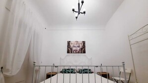 A bedroom with a white bed, a chandelier, a painting on the wall, and a white curtain. - Cozy apartment, ideal for families, in the heart of Ortigia (Siracusa)