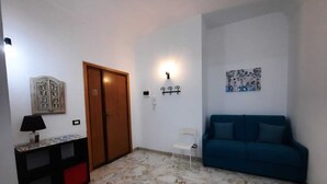 A living room with a blue sofa, a wooden door, a wall-mounted light fixture, and a decorative piece on the wall. - Cozy apartment, ideal for families, in the heart of Ortigia (Siracusa)