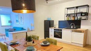 A modern kitchen with white cabinets, a black oven, and a wooden countertop. There is a dining table with green chairs and a hanging light fixture. - Sit back and relax with us between the Moselle and the vineyards. (Mehring)