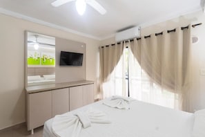 A hotel room with a bed, a TV mounted on the wall, a mirror, and a window with curtains.