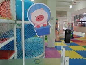 A play area with a pig-shaped bucket, a blue ball pit, and a colorful floor.