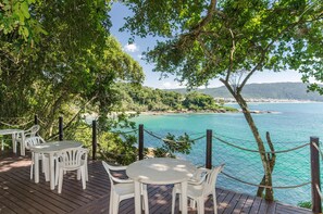 A wooden deck with white plastic chairs and tables overlooking a turquoise sea and a coastal landscape. - Bombinhas Tourist (Bombinhas)