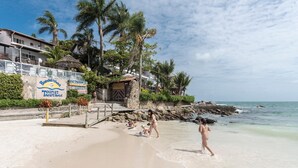A beach with a sign for the Bombiklas Tourist Art Hotel, palm trees, and a rocky shoreline. - Bombinhas Tourist (Bombinhas)