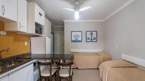 A compact kitchen with a microwave, a sink, and a ceiling fan. There are two chairs and a bed with patterned bedding. - Bombinhas Tourist (Bombinhas)