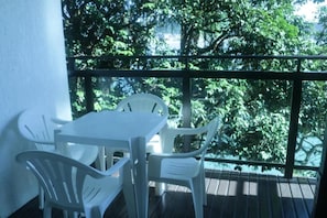 A balcony with a table and chairs, overlooking a lush green area.