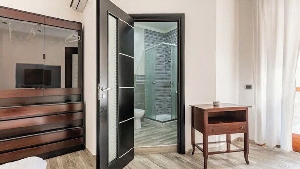 A modern bedroom with a wooden wardrobe, a glass door leading to a bathroom, and a small wooden nightstand. - CasaCondo 3 Apt: 5-Star Comfort, Conviviality & Privacy by UNESCO Heritage (Torre del Greco)