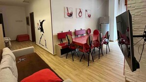 A modern living room with a dining area, wooden flooring, a grey sofa with red cushions, and a flat-screen TV mounted on the wall. - CasaCondo 3 Apt: 5-Star Comfort, Conviviality & Privacy by UNESCO Heritage (Torre del Greco)