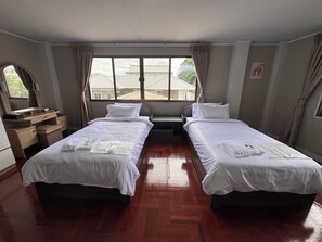 Ein Hotelzimmer mit zwei Betten, Holzböden, einem Schreibtisch mit Spiegel und einem Fenster mit Vorhängen.