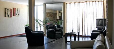 Ένας ευρύχωρος χώρος καθιστικού με μεγάλη τηλεόραση επίπεδης οθόνης, άνετα καθίσματα και θέα προς το εξωτερικό περιβάλλον.