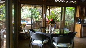 A covered outdoor seating area with a round table and chairs, surrounded by a wooden fence and lush greenery. - Ocean & Forest Views, Wildlife, Pool, Beach, Family & Friends, A/C....5 Star! (Uvita)