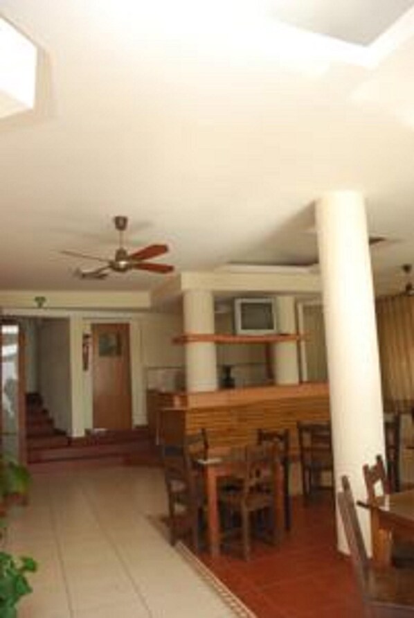 A spacious living room with a wooden dining table, chairs, a ceiling fan, and a television. - Gran Crisol Hotel (Córdoba)