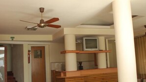 Ein Hotelzimmer mit Deckenventilator, einem Fernseher auf einem Holzregal und einer Tür mit der Aufschrift 'EXIT'.