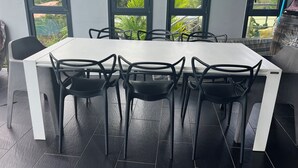 Comedor con mesa blanca y sillas negras, ventanas amplias que ofrecen vistas a zonas verdes y colinas.