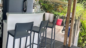 Un área de bar moderna al aire libre, con una encimera blanca y tres taburetes grises.