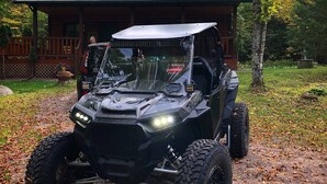 A Polaris RZR ATV parked in front of a wooden cabin with a deck.
