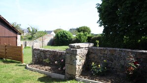 Un muro de piedra con un portón de madera, un área verde con flores y un edificio al fondo.