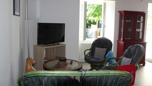 Una sala de estar con televisor, un mueble de madera y una silla con cojín.