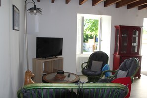 A living room with a television, a wooden cabinet, and a chair with a cushion.