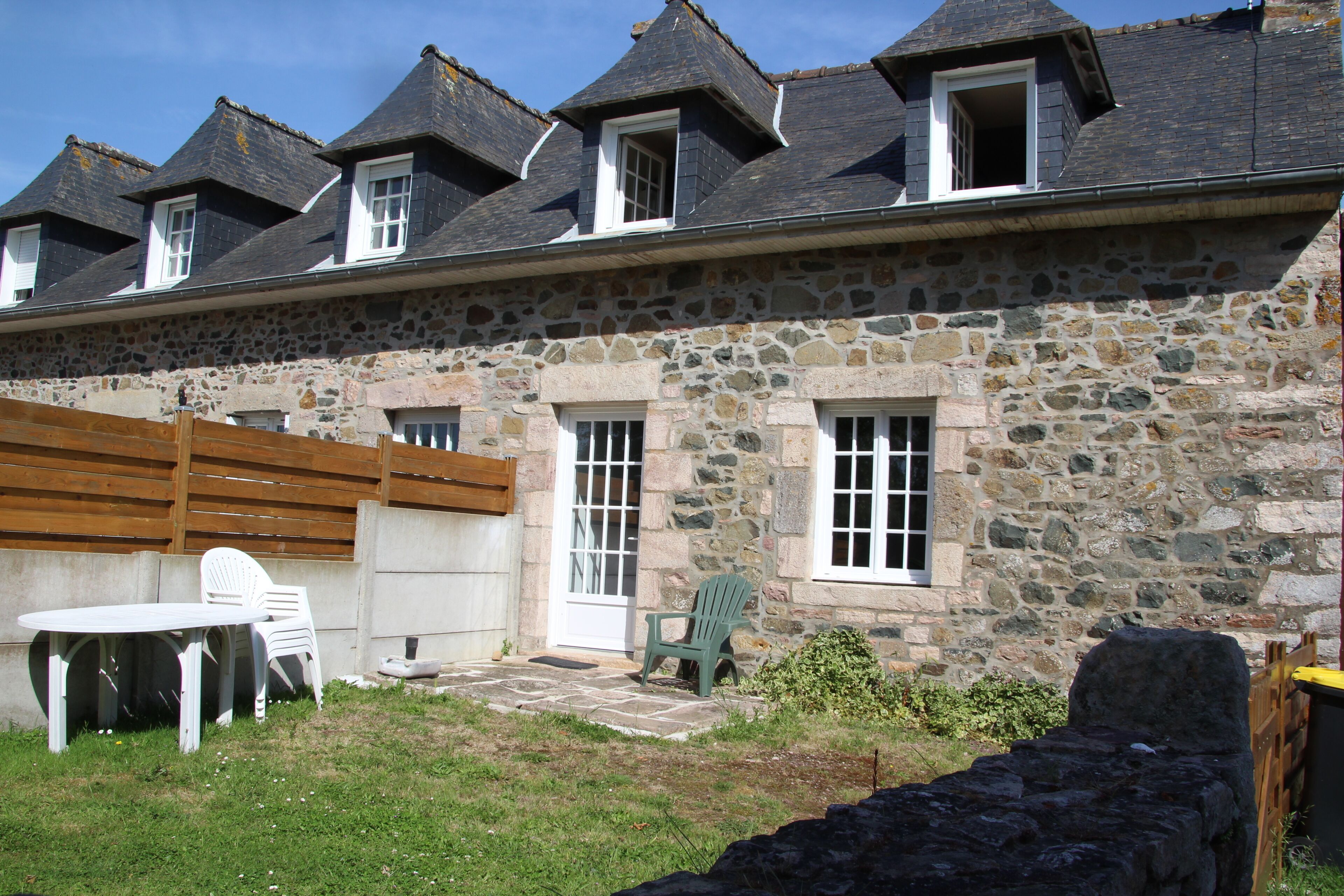 A stone building with a sloped roof, a wooden fence, and a small patio with outdoor furniture.
