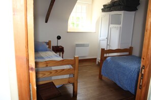 Un dormitorio con dos camas de madera, una mesita de noche pequeña, un radiador y una ventana con cortinas.
