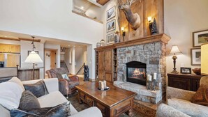 A spacious living room with a stone fireplace, wooden furniture, and a mounted deer head. - Villa Montane 226 - 4 Bedroom (Beaver Creek)