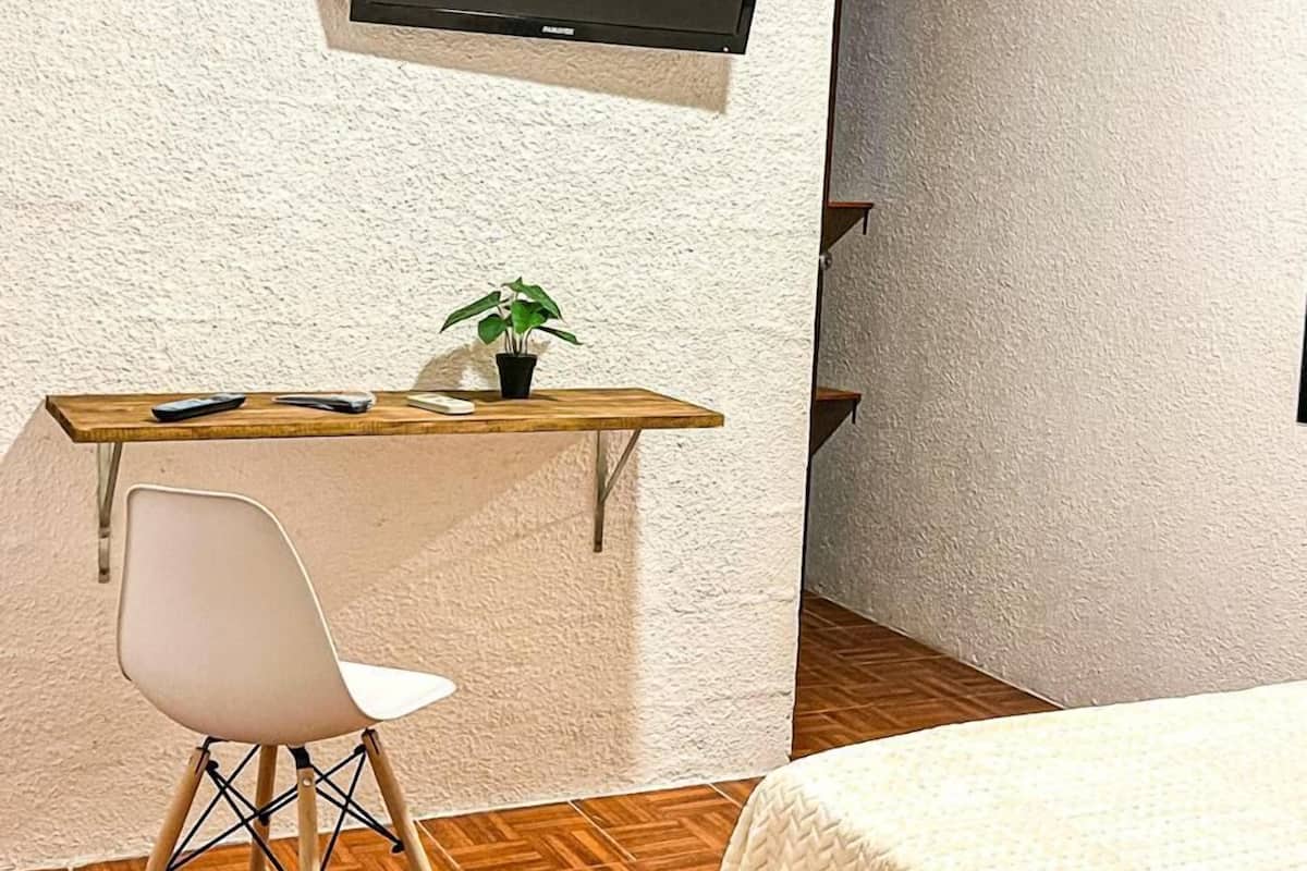A room with a bed, a desk with a chair, a television mounted on the wall, and an air conditioning unit.