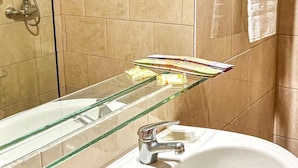 A bathroom with a glass shelf holding toiletries, a white sink, a glass shower enclosure, and a towel rack. - Eco Suite (Treinta y Tres)