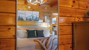 A wooden interior with a bed, pillows, a blanket, and framed pictures on the wall. - Romantic Hideaway • Hot Tub, Scenic Views, Dogs OK (Pigeon Forge)