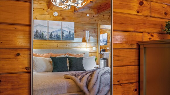A wooden interior with a bed, pillows, a blanket, and framed pictures on the wall.
