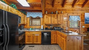A wooden cabin kitchen with a black refrigerator, wooden cabinets, a sink, and a dishwasher.