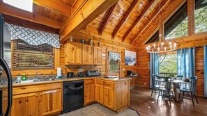 A wooden cabin interior with a kitchen, dining area, and a large window.