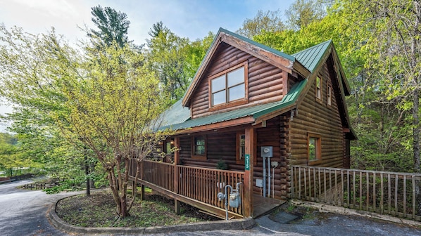 A log cabin with a porch, surrounded by trees.