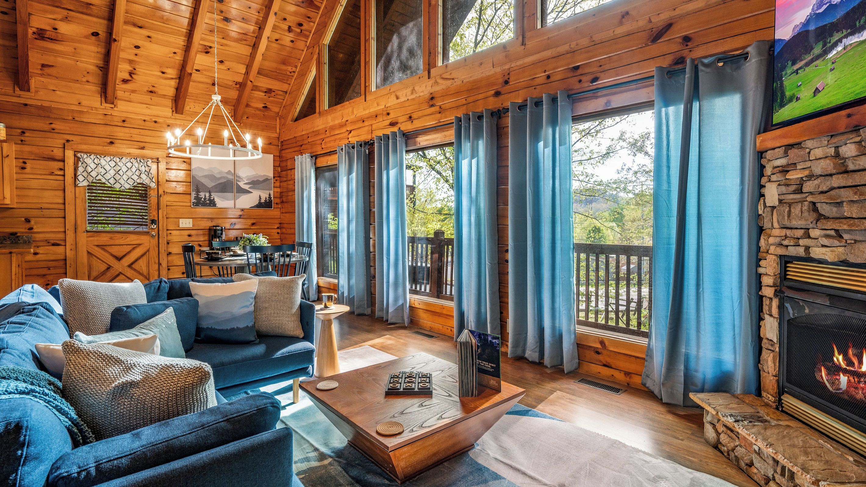 A cozy cabin interior with a fireplace, a dining area, and large windows.