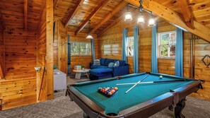 Uma cabana de madeira com mesa de bilhar, sofá e uma pequena mesa com uma planta.