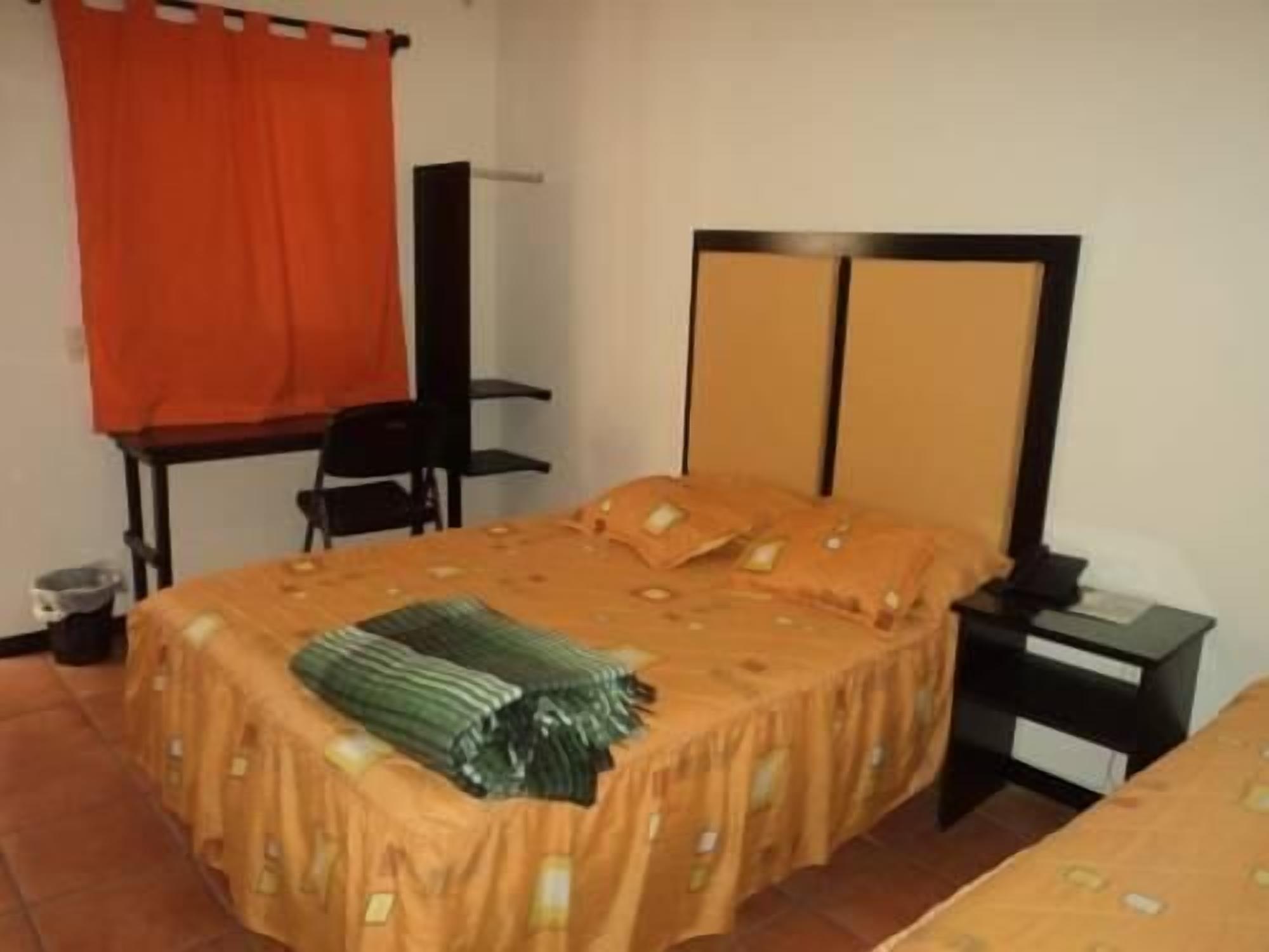Una habitación con cama, una silla, una mesita pequeña y una mesita de noche.