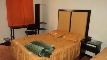 Una habitación con cama, una silla, una mesita pequeña y una mesita de noche.