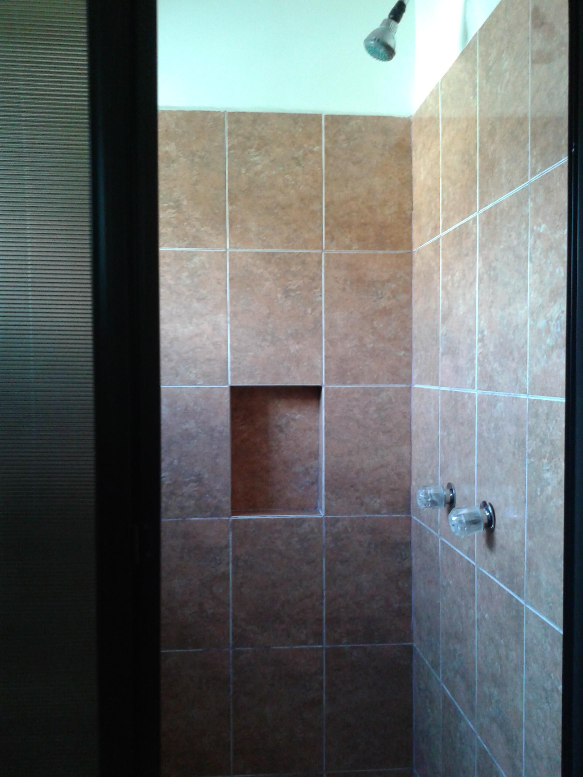 Ducha con azulejos marrones y puerta de cristal.