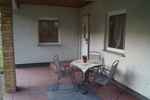 A covered patio with a table and four chairs, a potted plant, and two windows. - Schones Ferienhaus im Nationalpark Granitz (Zirkow)