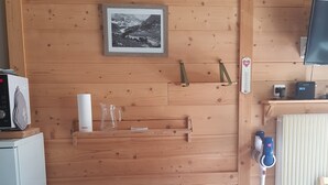 Un interior de madera con una mesa, sillas, un refrigerador, un microondas, una tetera y un cuadro enmarcado en la pared.