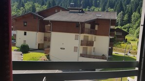 Un balcón con mesa y sillas, con vistas a una hilera de casas y una colina boscosa al fondo.