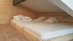 Una habitación pequeña de madera con dos literas, piso de madera y techo inclinado.