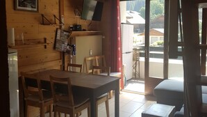Un interior de madera con una mesa de comedor, sillas, un televisor y una ventana que ofrece vistas a edificios.