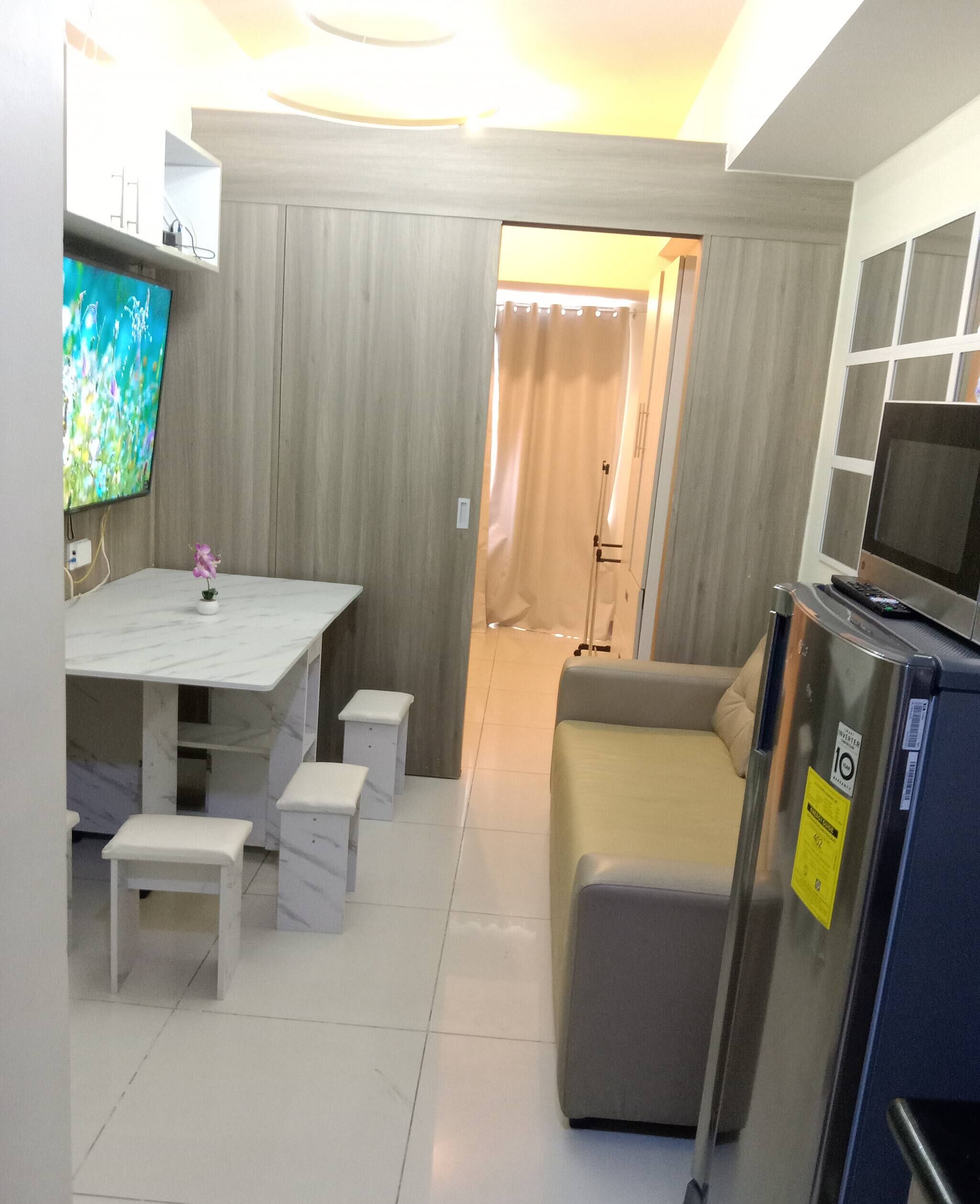 A compact living space with a TV, a sofa, a small table, and a refrigerator.