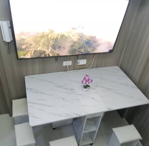 Una habitación con un televisor de pantalla plana grande montado en la pared, una mesa de mármol blanco y una pequeña orquídea en maceta.