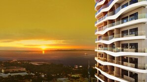 A high-rise building with multiple balconies, a sunset view, and a distant shoreline.